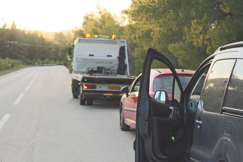 A roadside scene depicting a car with a technical issue being assisted by a towing vehicle, with warning triangles set up for safety