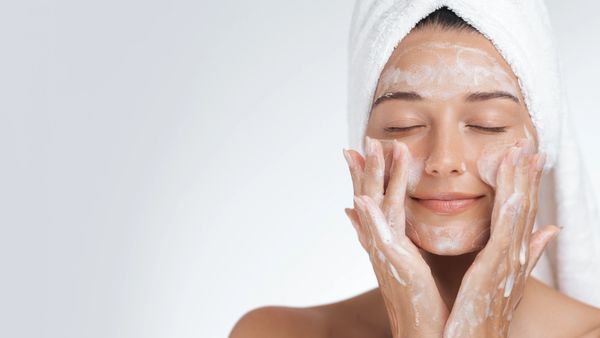 Woman with a towel on her head washing her face with foam cleanser.
