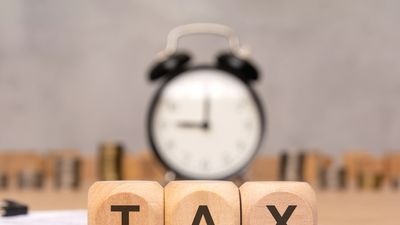 Wooden blocks spelling TAX with clock and coins in background.