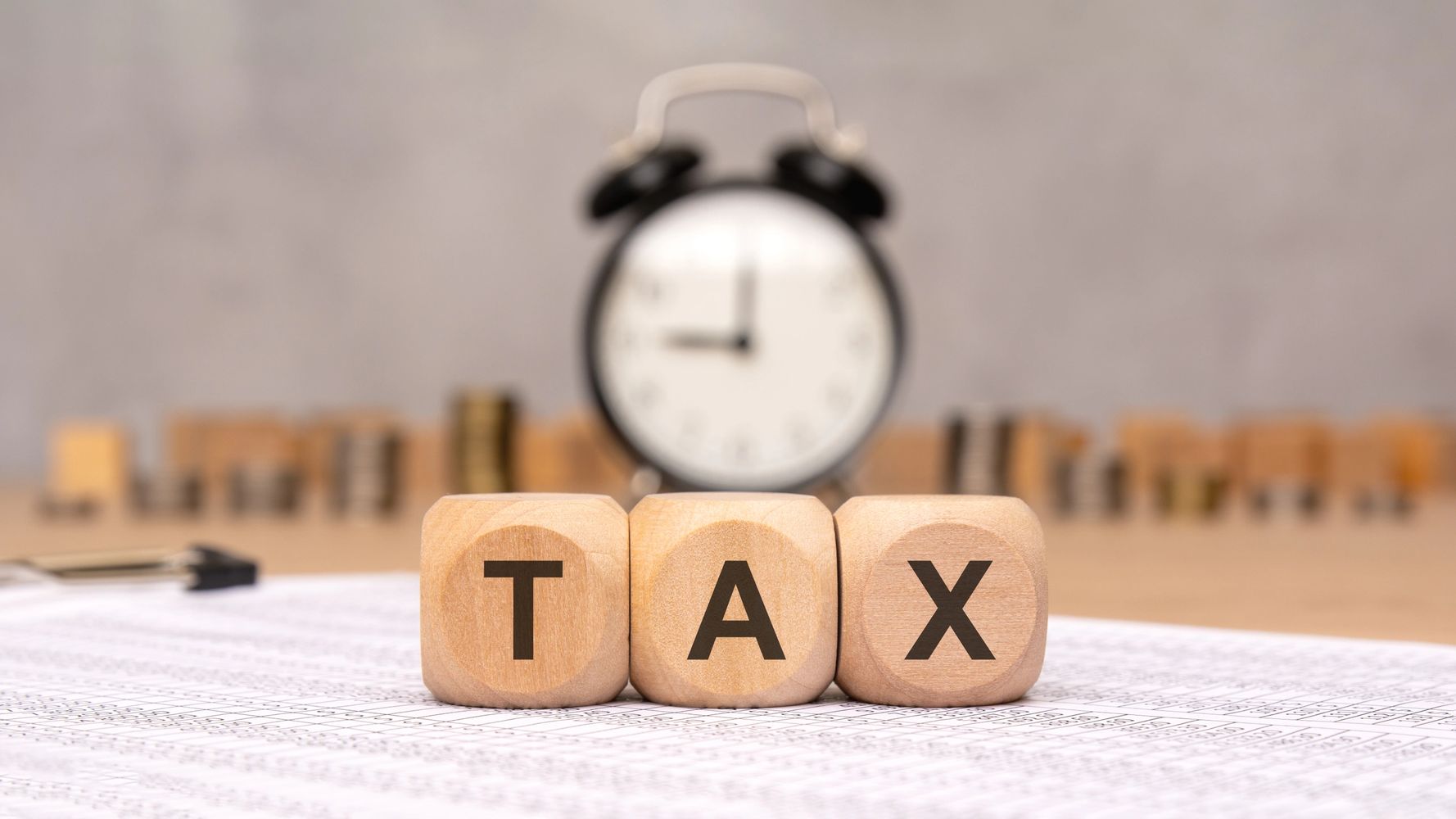 Wooden blocks spelling TAX with clock and coins in background.
