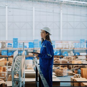 Woman engineer in blue uniform and helmet inspecting warehouse inventory.