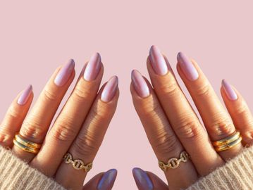 Hands with long, glossy lavender nails and gold rings against a soft pink background.