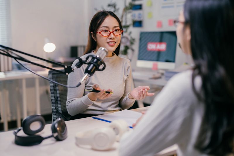 Two young female podcasters are recording a new episode in their brightly lit studio, discussing current events and sharing their insights with their audience
