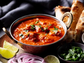 A bowl of rich butter chicken curry garnished with cilantro and lime wedges.