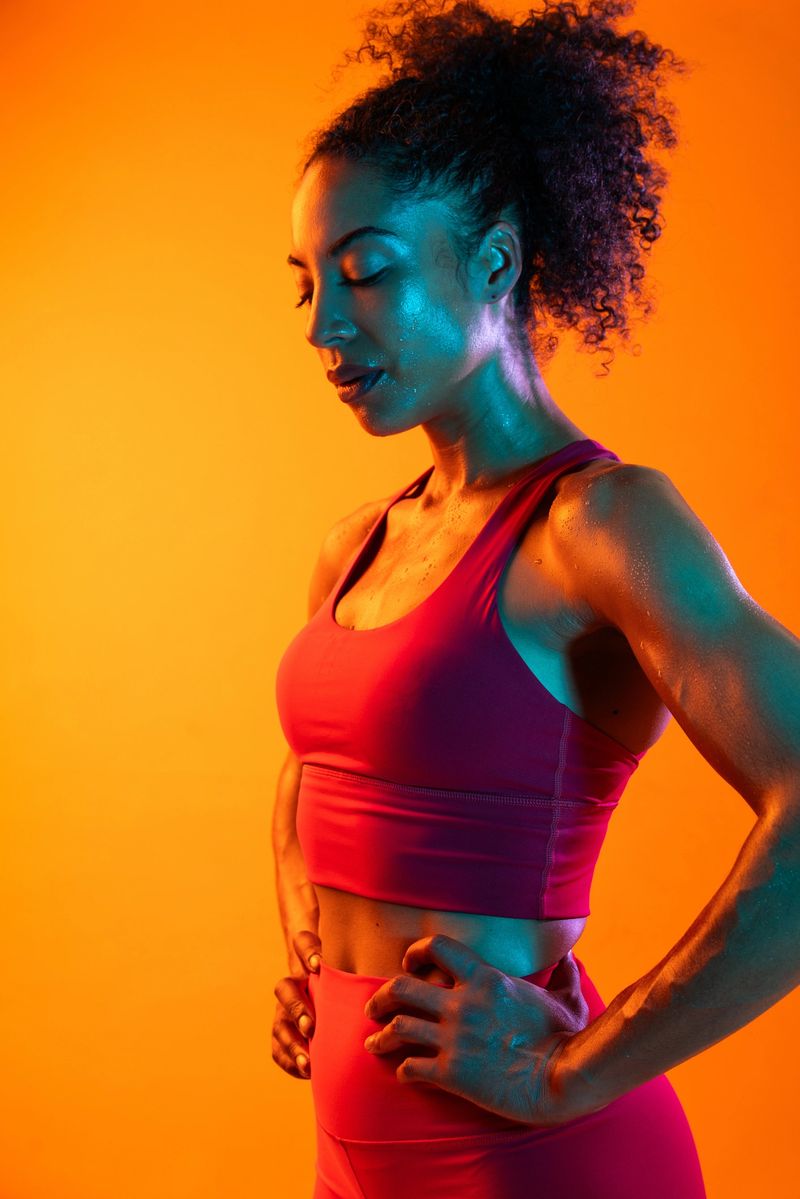 Sportive black hispanic woman wearing sportswear training in fitness studio, colorful dramatic lighting - African-american female athlete doing sport workout