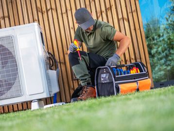 Technician repairing an outdoor air conditioning unit with tools in a bag.