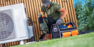 Technician repairing an outdoor air conditioning unit with tools.
