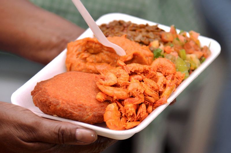 Acaraje. Traditional Brazilian food made with vatapá, caruru and dried shrimp. A person carrying a small plate of Acarajé