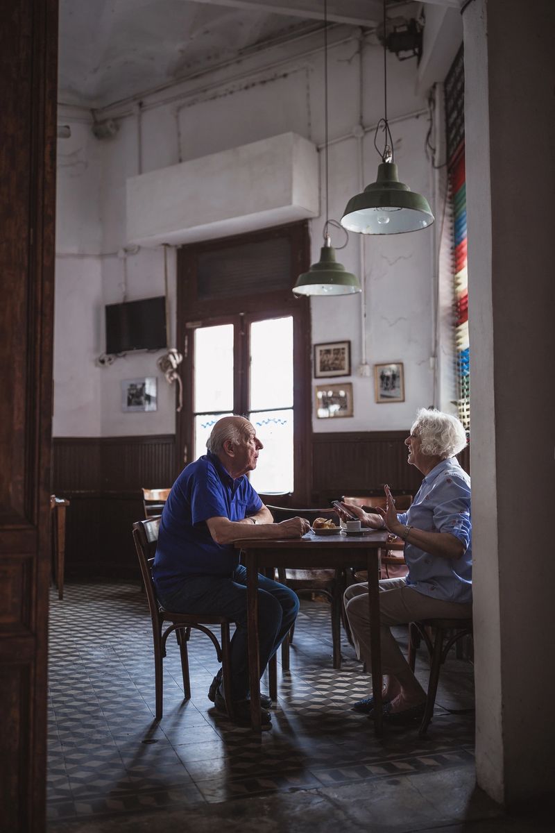 Elderly couple enjoying a small café, captured in the late afternoon. The setting is rustic with a vintage vibe, highlighting a quiet and intimate atmosphere.