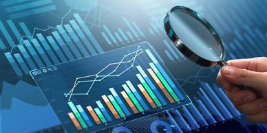 Hand holding magnifying glass over digital financial charts and graphs.