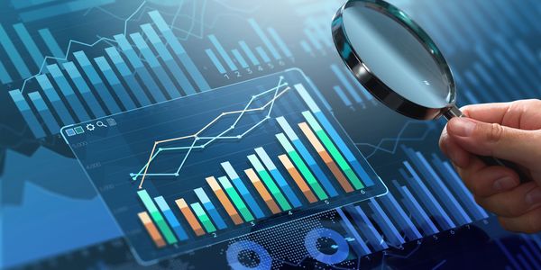 Hand holding magnifying glass over digital financial charts and graphs.