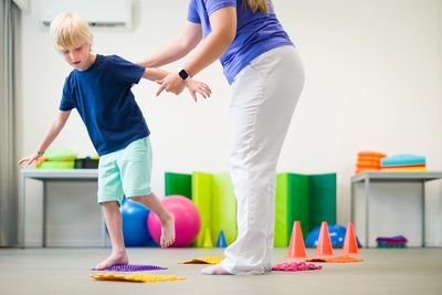 Child balancing with adult assistance in a therapy session.