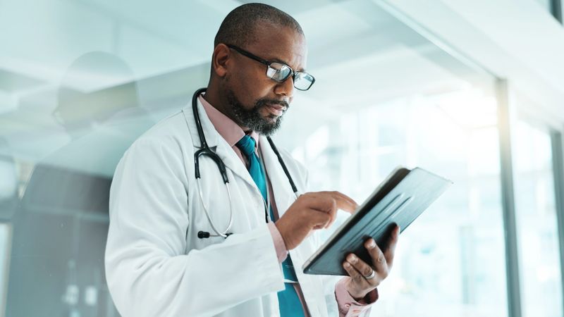 Black man, doctor and tablet for healthcare in hospital with medical research, Telehealth and surgery schedule. Male surgeon, reading and digital for history report, patient information and diagnosis