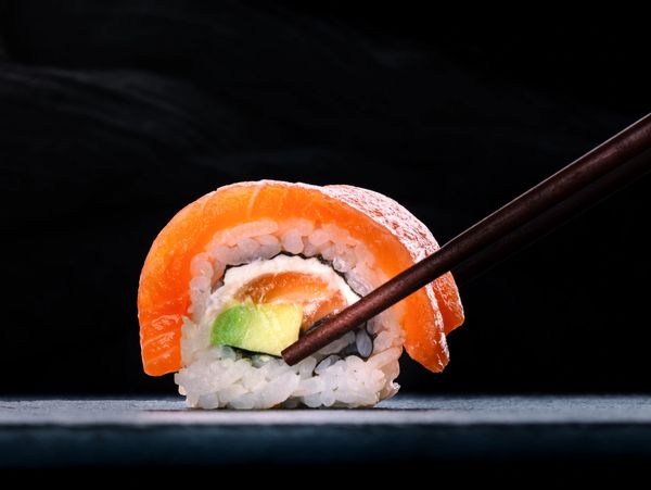 Close-up of sushi with chopsticks on a dark background.