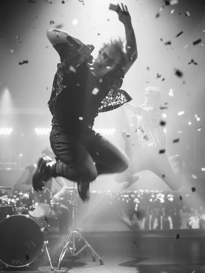 Energetic musician jumps mid-air during a lively concert with confetti falling.