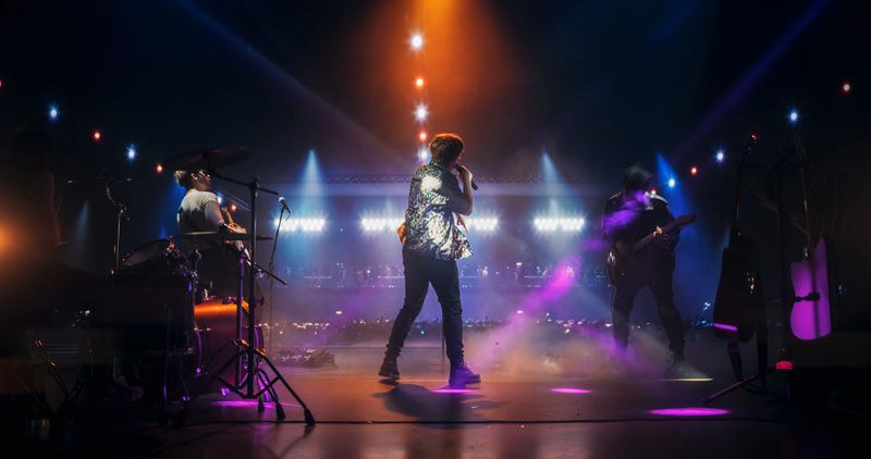 Professional Rock Musicians Performing a Live Set on Festival Stage, Playing Popular Rock Tracks in Front of a Crowded Arena with Falling Confetti. Electrifying Performance at an Indoors Festival
