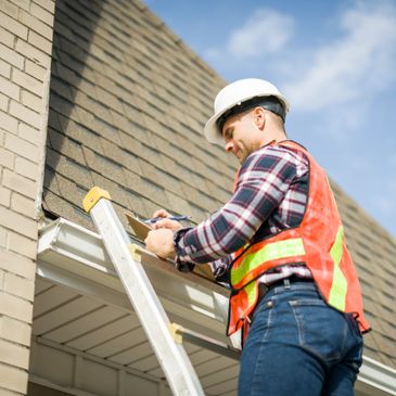 Construction worker inspecting house roof on ladder with clipboard.