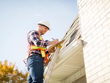Construction worker on a ladder inspecting a house exterior.