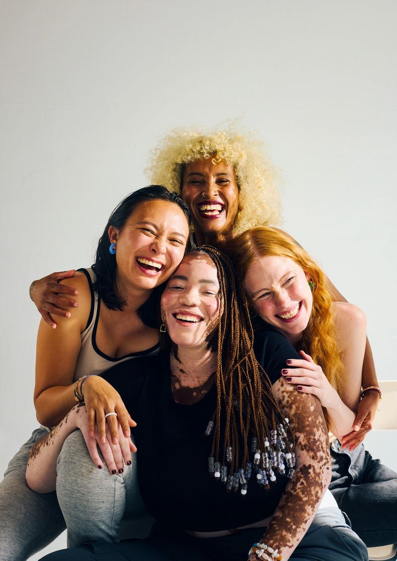 Four diverse Gen Z women embracing and laughing together. Beauty and wellness concept.