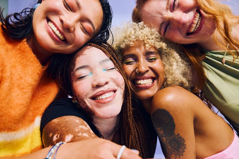 Four diverse Gen Z women embracing and smiling with eyes closed