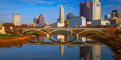 City skyline with bridge reflected in calm river on clear day.