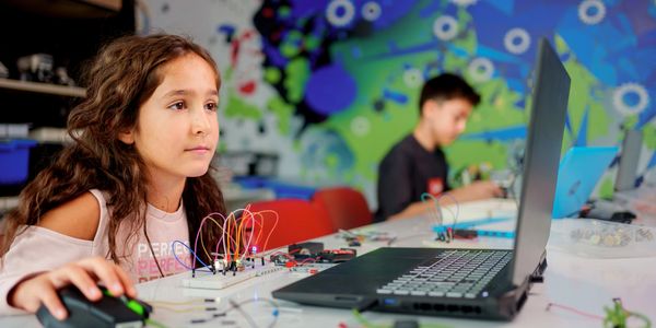 Young girl engaged in electronics project with laptop in classroom.