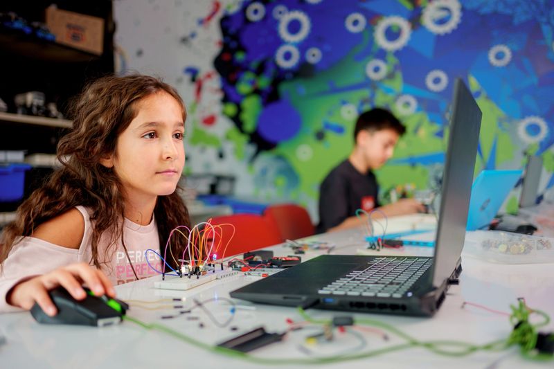 A female student participating in a hands-on robotics and STEM education activity. The child is working on coding and programming using laptops while assembling a robot with various components. The classroom is lively and full of educational tools and materials that stimulate creativity and innovation. Perfect for themes related to technology, education, learning and the development of future skills.