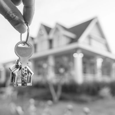 Hand holding house-shaped keys in front of a house.
