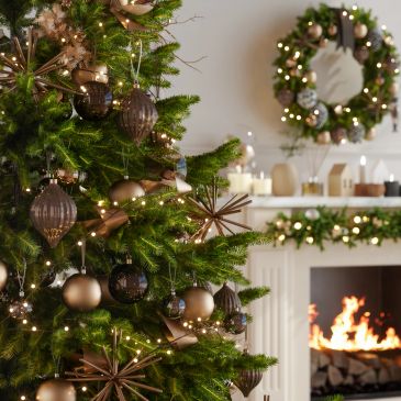 Decorated Christmas tree with fireplace and wreath in the background.