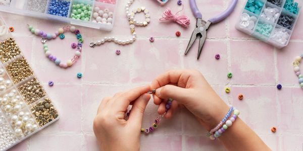 Hands making beaded jewelry with colorful beads and tools.