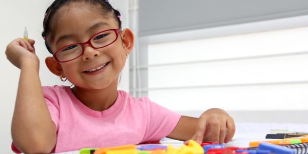 Smiling girl with red glasses playing with colorful educational toys.