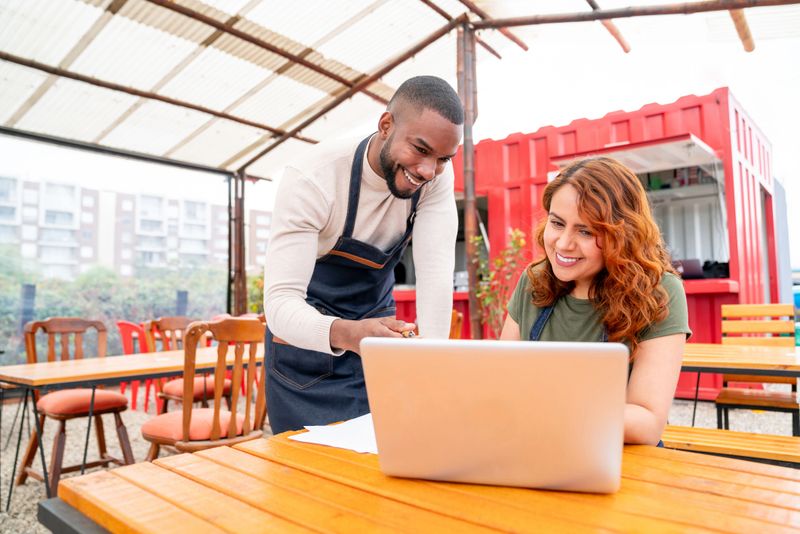 Happy waiter talking to a business manager at a restaurant while doing the accountancy and smiling