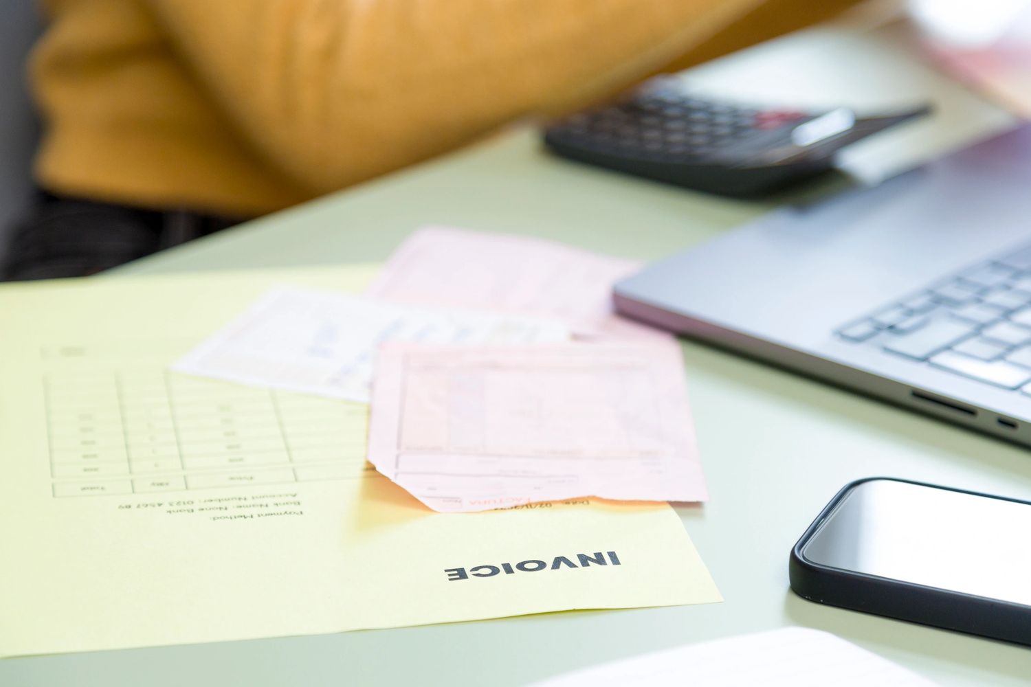 Workspace with an invoice, calculator, laptop, and smartphone on a desk.