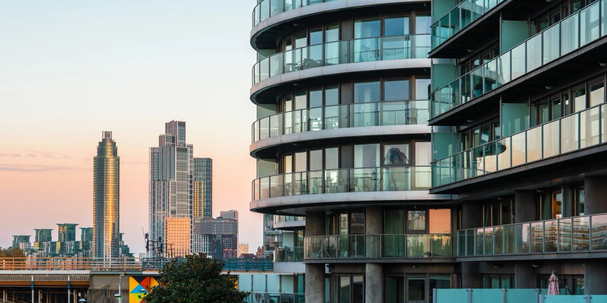Modern cityscape with glass balconies and skyscrapers at sunset.