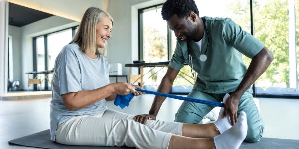 Therapist helping woman with leg exercises using resistance band.