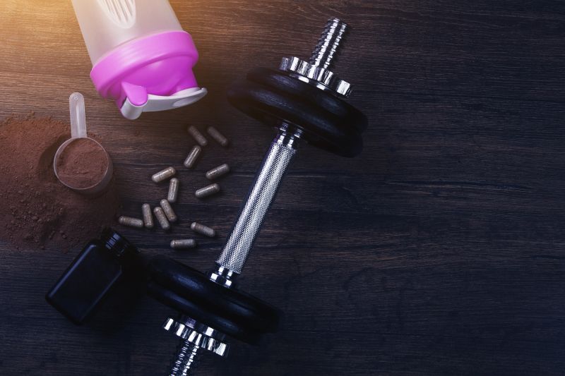 Fitness Supplements, Dumbbell, and Protein Shaker on Wooden Surface.