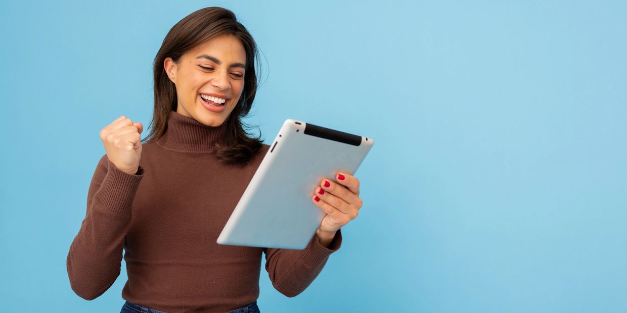 Happy woman celebrating while using a tablet against a blue background.