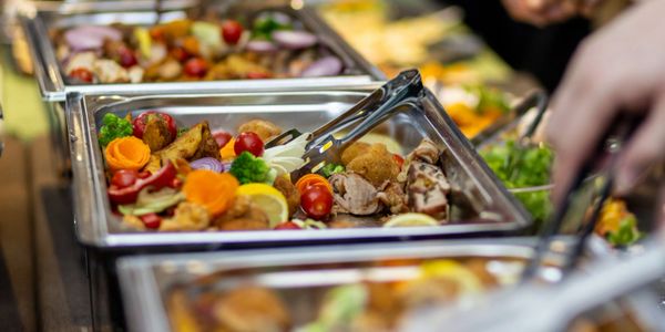 A buffet with trays of assorted cooked foods and fresh vegetables.
