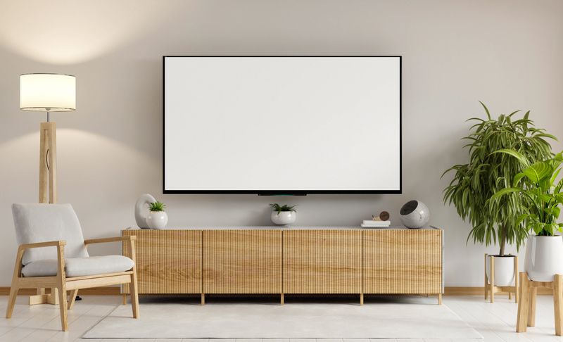 Living room with a white wall and a large flat screen television. The television is turned off and the room is empty- 3D rendering
