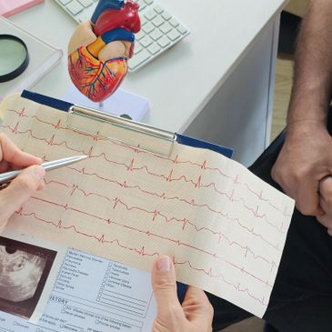 Doctor explaining an ECG report to a patient with a heart model nearby.