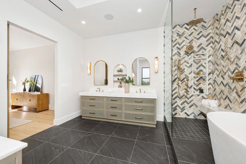 Modern bathroom interior with stylish decor, featuring a double vanity, herringbone tile shower, and sleek black flooring.