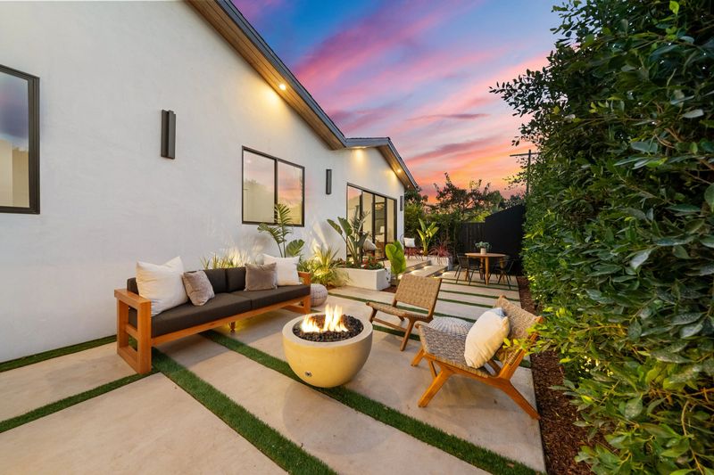 Modern backyard patio with cozy seating and fire pit at sunset, featuring a vibrant sky and lush greenery.