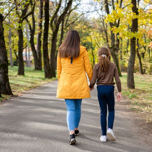A woman and a girl walk hand in hand in a park during autumn.