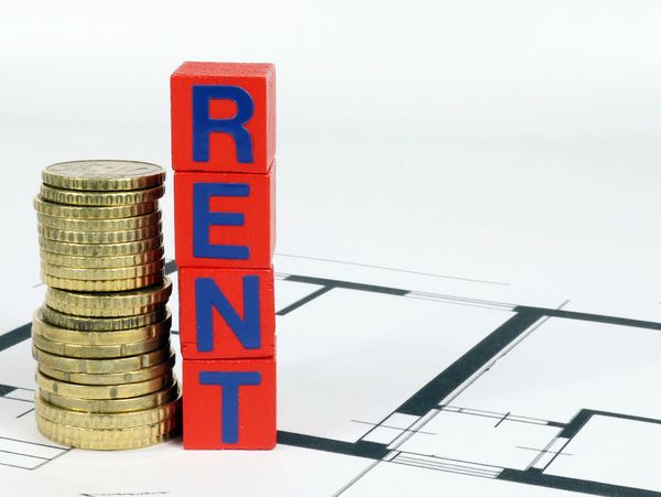 Stack of coins next to blocks spelling RENT on a blueprint.