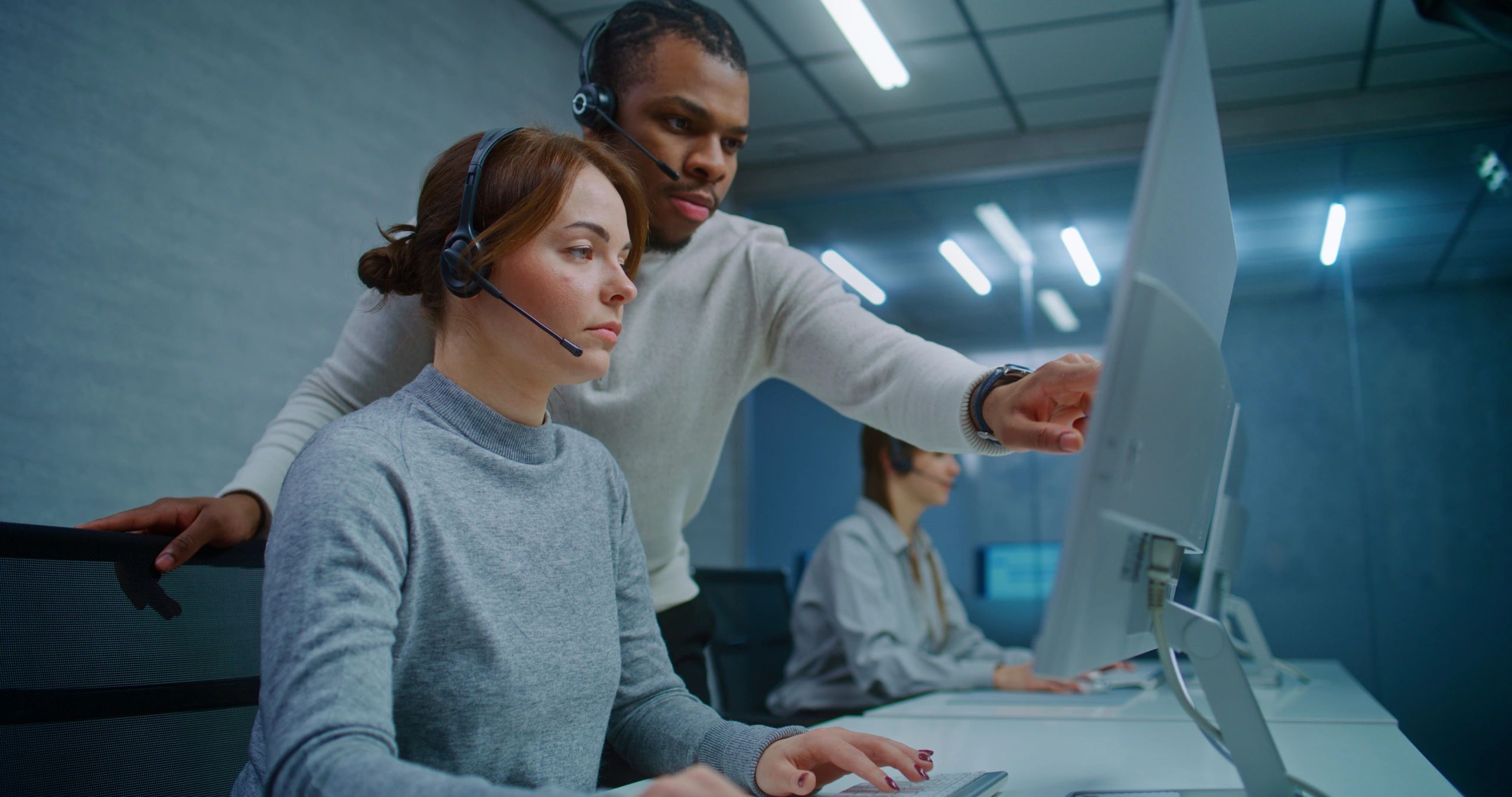 Man instructing woman at a computer in a call center.