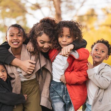 A joyful group of children and a young woman hugging outdoors in autumn.