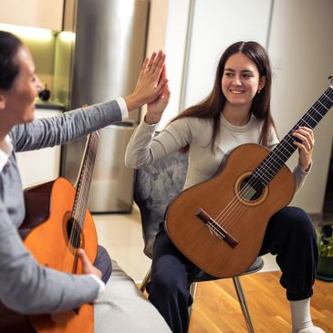Two people with guitars sharing a high-five during a music session.