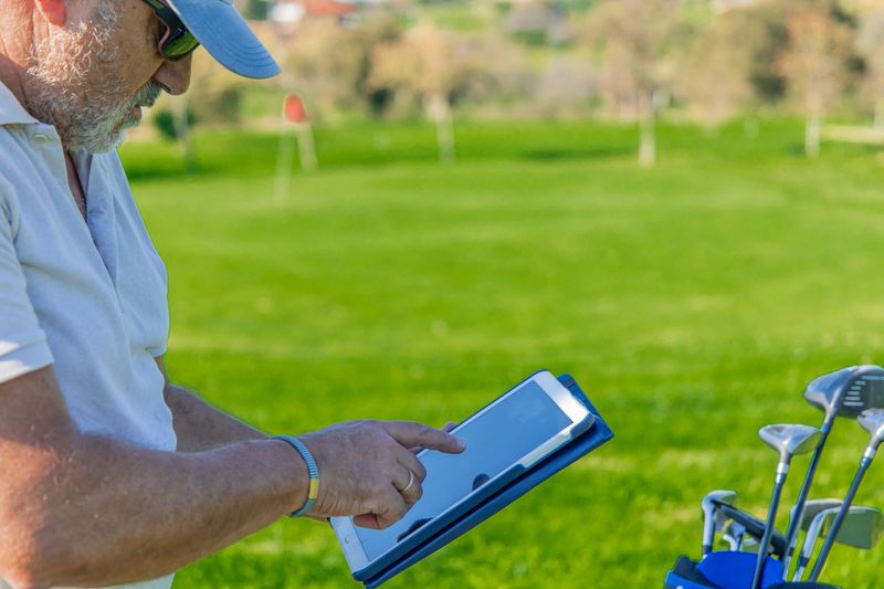 elderly golfer is marking points on a tablet during a golf tournament, demonstrating how apps are modernizing the sport