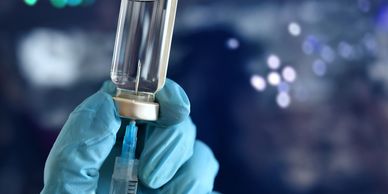 Gloved hand drawing liquid from a vial into a syringe.