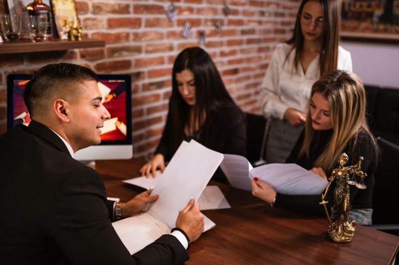 A lawyer holds legal documents while engaging in a discussion with clients in his office. The professional setting, combined with attentive conversation, reflects a focused consultation as they go over important case details.